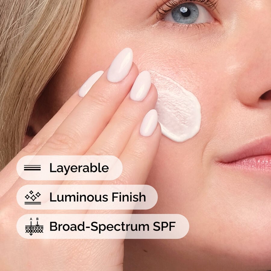 Woman applying a layerable, broad-spectrum SPF product with a luminous finish to her face.